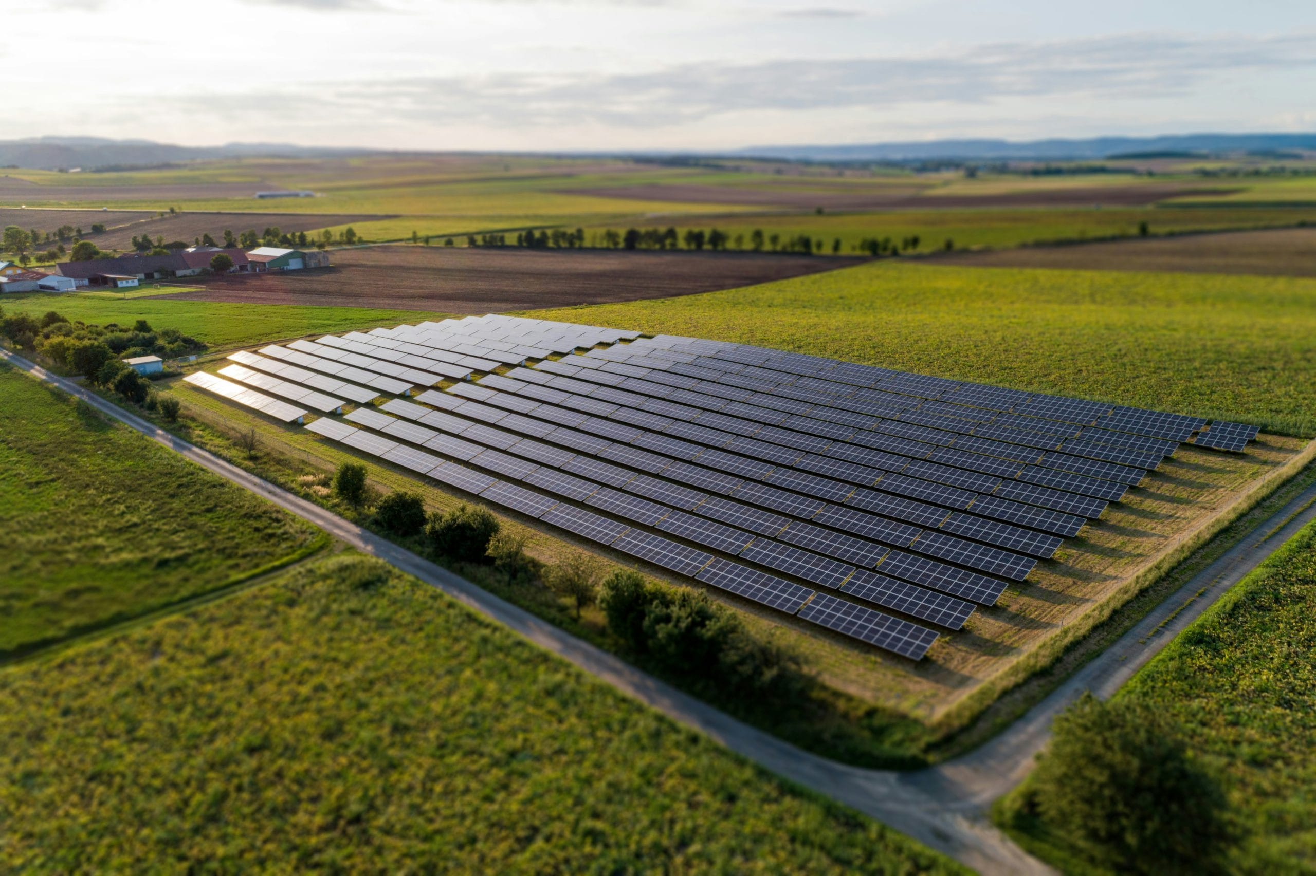 A green valley with a field of solar panels on it, shimmering.